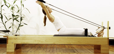 Wooden Pilates reformer used by a Pilates practitioner doing rowing exercise